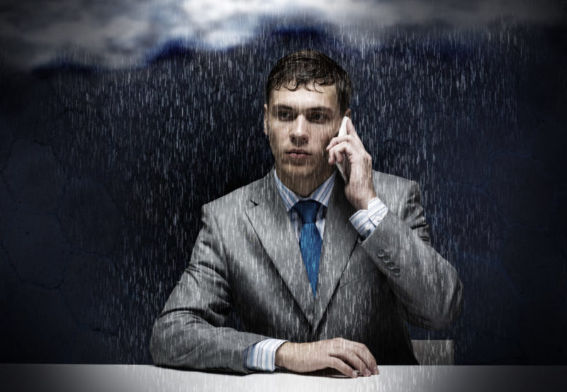 Un hombre está hablando por teléfono mientras cae lluvia, representando los comentarios negativos sobre su empresa