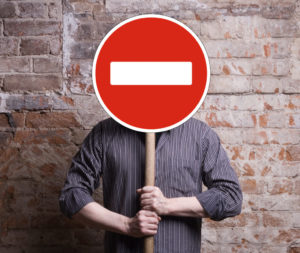 En la foto aparece un hombre que se tapa la cara con la señal de "prohibido" que sujeta entre las manos