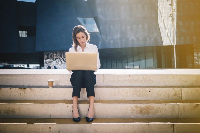 En la foto se ve a una chica sentada en unas escaleras trabajando en su ordenador