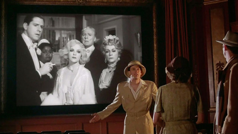 En la foto se ve a tres personas que discuten delante de una pantalla de cine en la que se ve una foto en blanco y negro
