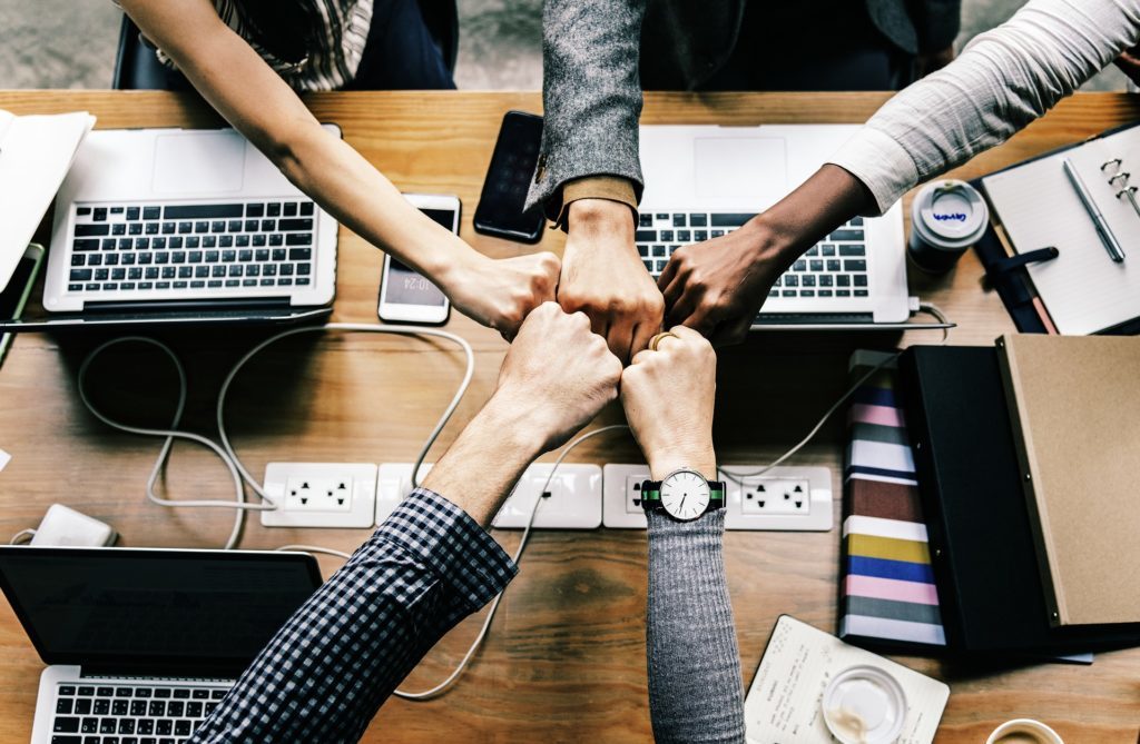 En la foto se ven los puños de cuatro personas, que se están juntando, como símbolo de trabajo en equipo